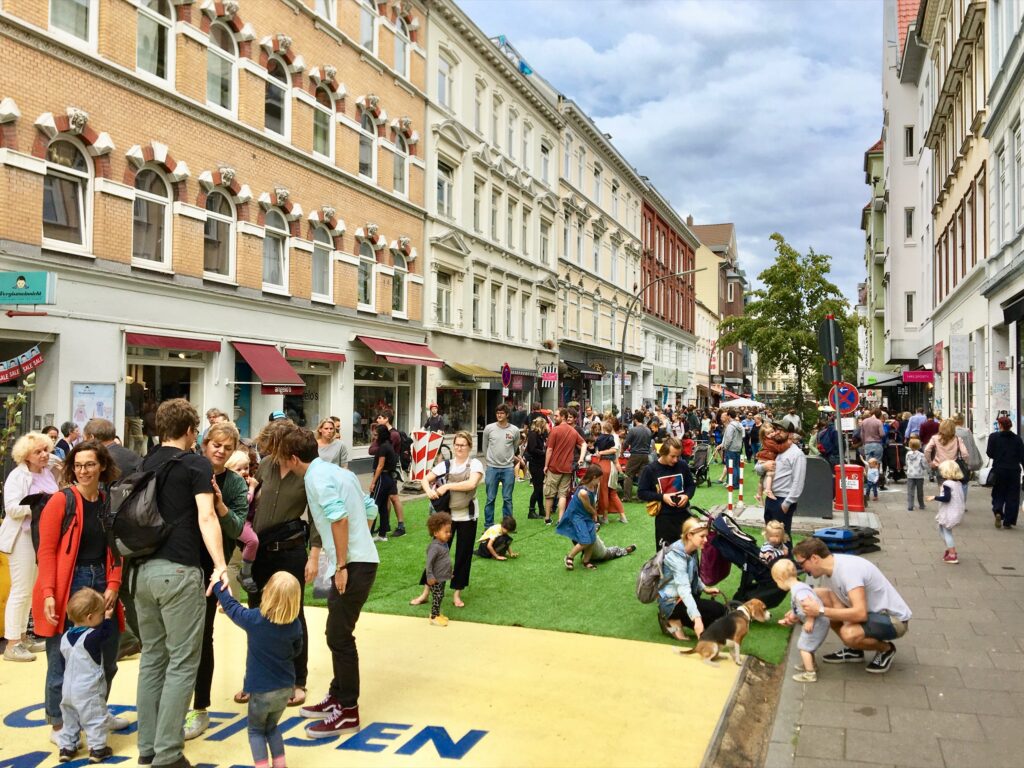 Viele Menschen, Familien und Kinder verweilen auf einer bunt bemalten Straße in der Innenstadt.