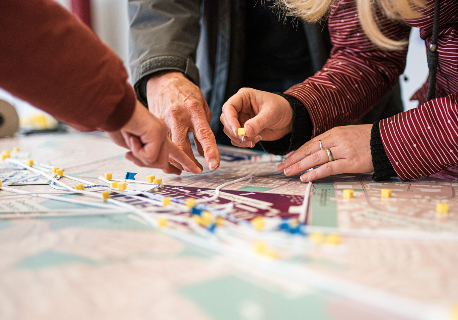 Nahaufnahme mehrerer Hände, die kleine gelbe Markierungen auf einem Stadtplan platzieren