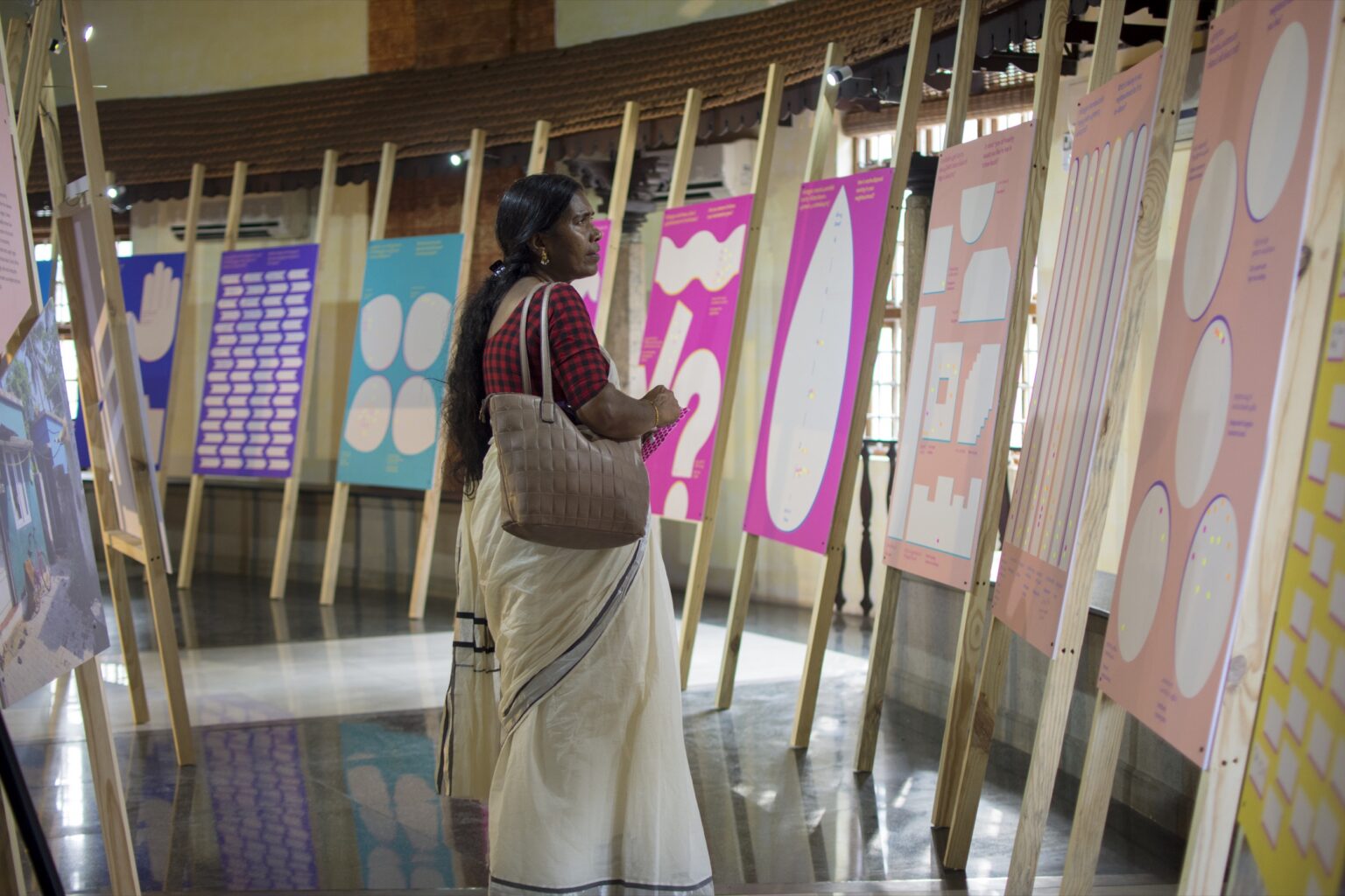 Frau betrachtet bunte Infotafeln auf einer Ausstellung im Innenraum.