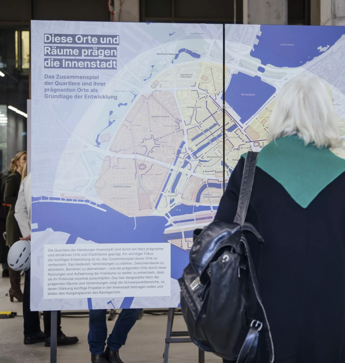 Besucherin betrachtet in einer Ausstellung eine große Karte der Hamburger Innenstadt mit dem Titel ‚Diese Orte und Räume prägen die Innenstadt‘.